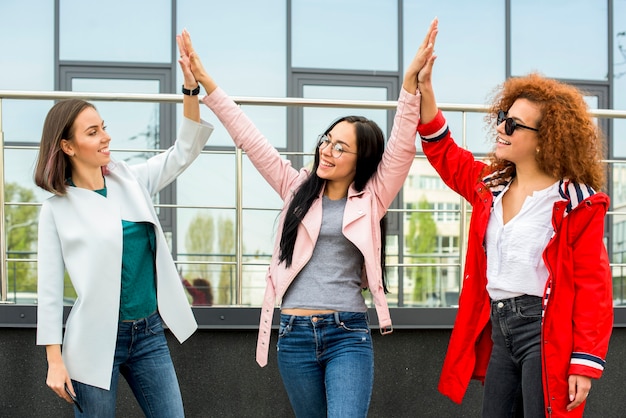 Free photo three fashionable female friends giving high five at outdoors