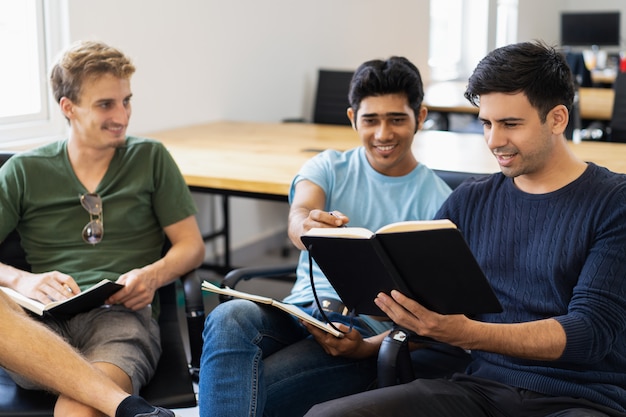 Free photo three fellow students studying, reading textbooks and talking