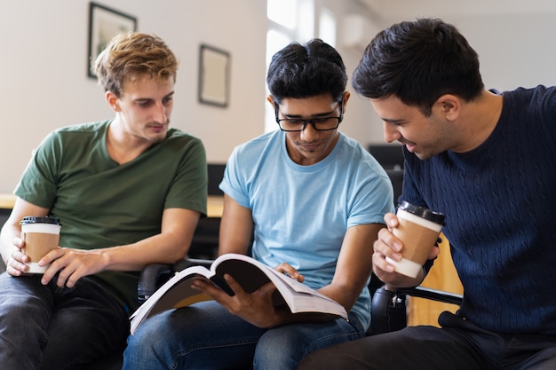 Three focused students studying together and drinking