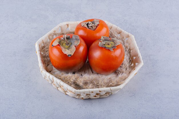 Three fresh ripe persimmon fruits in wicker basket.