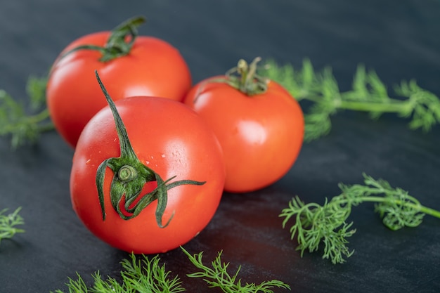 Three fresh tomatoes with greens on a dark surface.