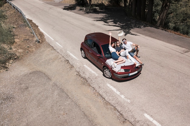 Three friends sitting on car hood enjoying the trip