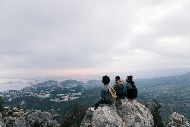 Free Photo three friends sitting on the top of mountain enjoying the scenic view