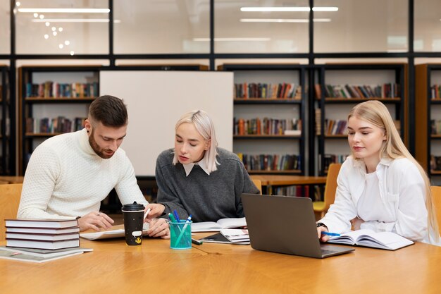 Free Photo three friends studying from documents and a laptop in a library