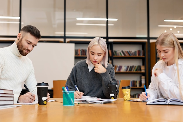 Free photo three friends studying from documents and notebooks in a library