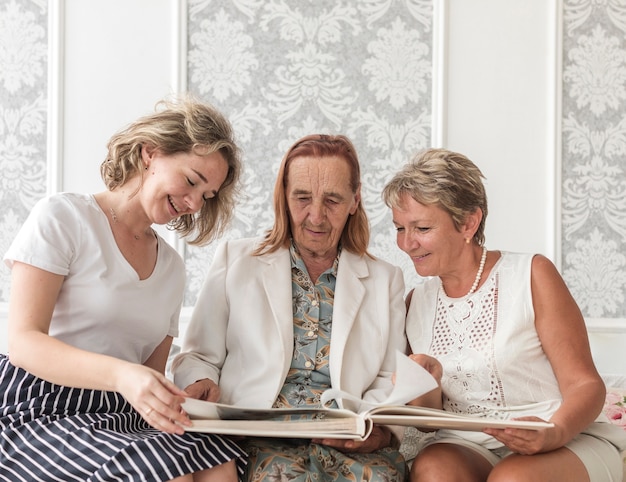 Free photo three generation women looking photo album while sitting on sofa