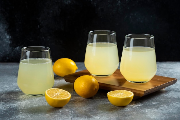 Free photo three glass cups with lemon juice on wooden board.