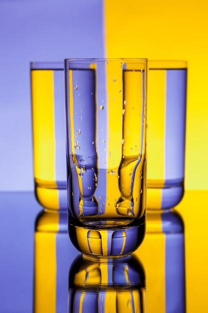 Free Photo three glasses with water over purple and yellow wall