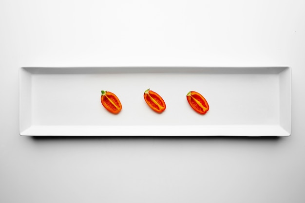 Free Photo three half of small sweet red pepper isolated in center of white plate