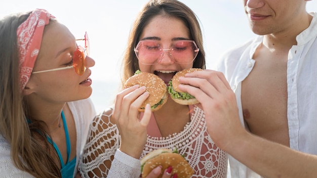 Three happy friends eating burgers together outdoors