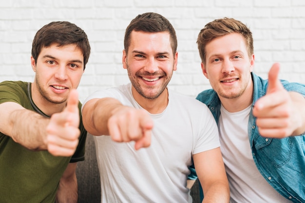 Three happy male friends pointing finger toward camera