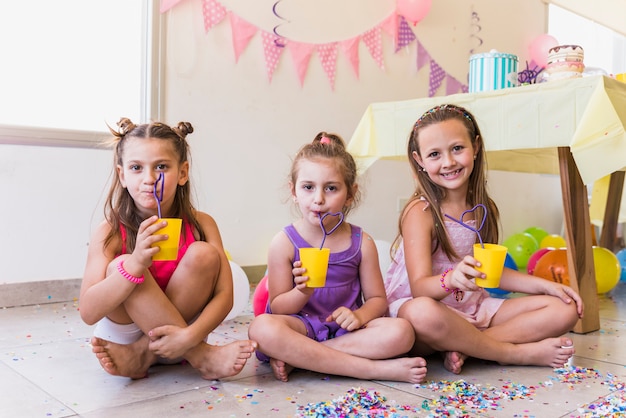 Three little girls drinking juice while celebrating birthday party at home