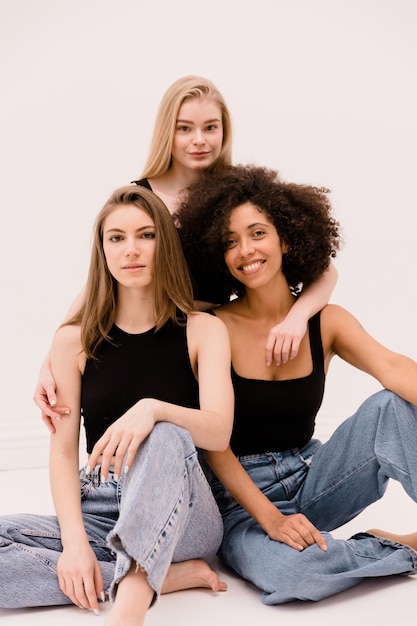 Three nice young interracial women of light and dark hair in black tops and jeans look at camera on white background