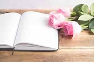 Free photo three pink roses with an open blank diary on wooden table