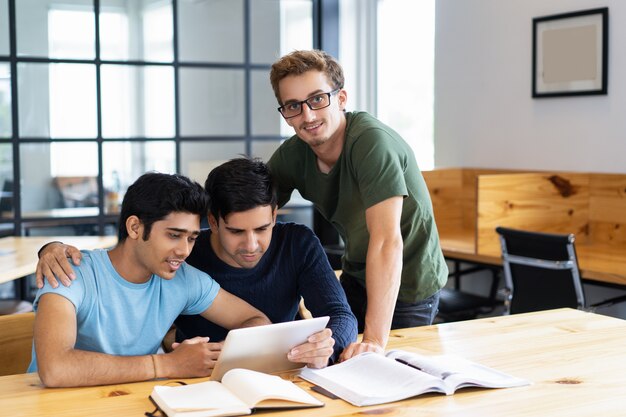 Three positive students browsing on tablet computer together