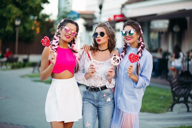 Three pretty and fashionable girls holding candies heart on stick