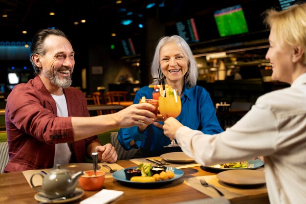 Three senior friends talking at a restaurant while cheering with drinks