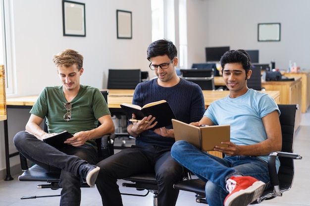 Three smiling fellow students studying and reading textbooks