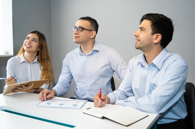 Three smiling young business colleagues sitting at meeting