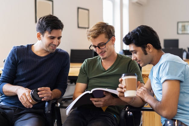 Three students reading textbook together and drinking