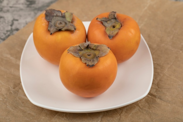 Free Photo three tasty fuyu persimmon on white plate on marble surface