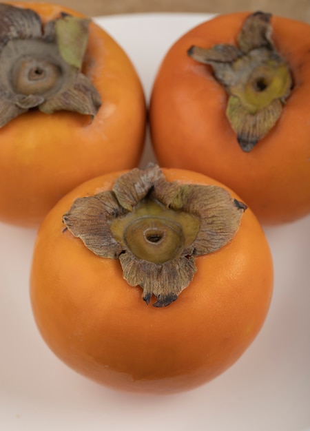 Free photo three tasty fuyu persimmon on white plate on marble surface