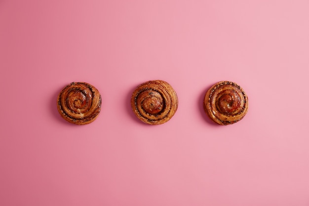 Three tasty soft buns with aromatic smell, bought in bakers shop, isolated on pink background. Rolls with sugar. Bakery for recipe book. Tasty sweet food, desserts. Above shot. Baked pastry.