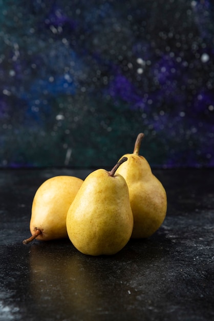 Three tasty yellow pears placed on black surface. 