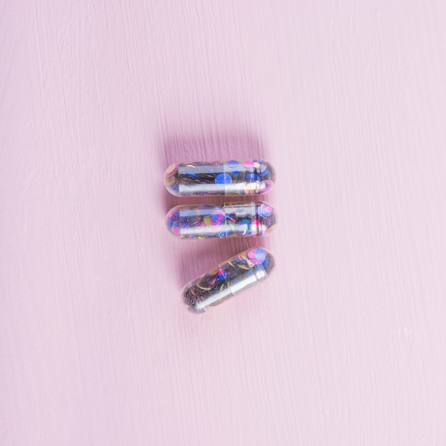 Free photo three transparent sequin capsules on wooden texture pink backdrop