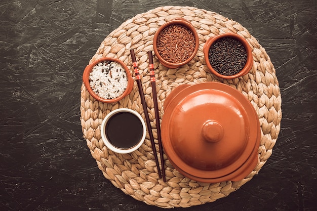 Three uncooked rice grain bowls with soya sauce; chopsticks on placemat