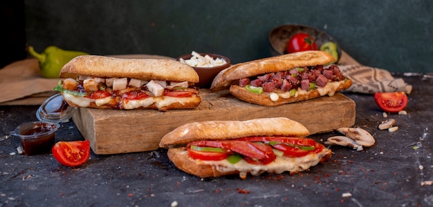 Three various baguette sandwiches with mixed foods on a stone table