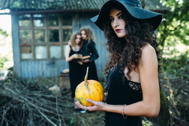 Free photo three vintage women as witches, pose in front of an abandoned building on the eve of halloween