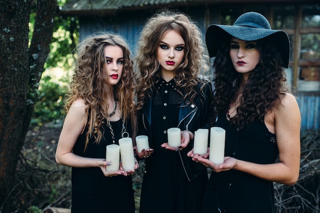 Three vintage women as witches, poses and hold in their hands the candles on the eve of Halloween