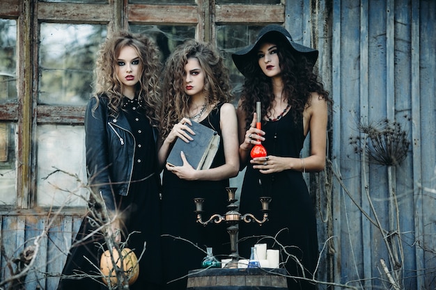 Three vintage women as witches, poses near an abandoned building on the eve of Halloween