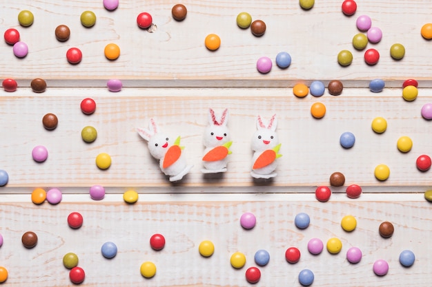 Three white bunnies in the center with colorful gem candies on wooden table