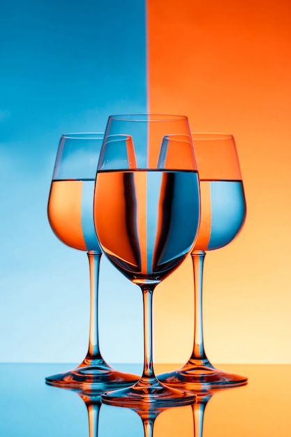 Free photo three wineglasses with water over blue and orange wall