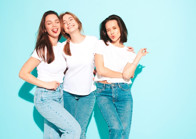 Three young beautiful smiling hipster female in trendy same summer white t-shirt and jeans clothes