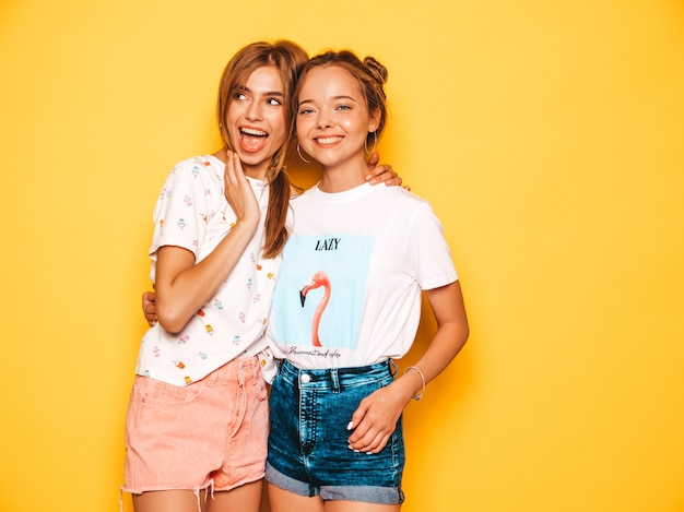 Free Photo three young beautiful smiling hipster girls in trendy summer clothes. sexy carefree women posing near yellow wall. positive models going crazy and having fun. in sunglasses