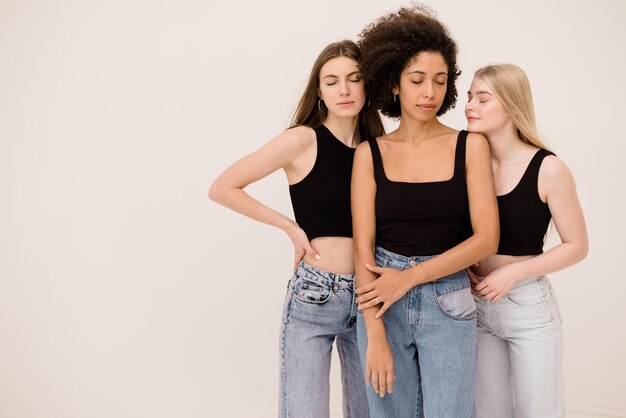 Three young multiracial young women with different skin types with their eyes closed stand on white background with space for text