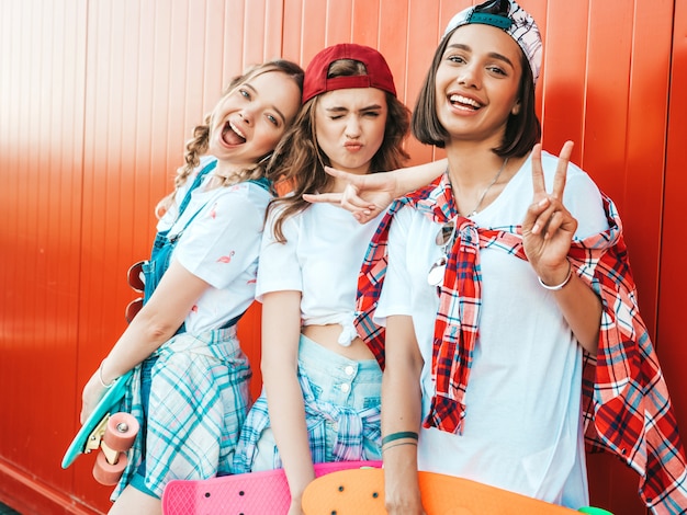 Free photo three young smiling beautiful girls with colorful penny skateboards.