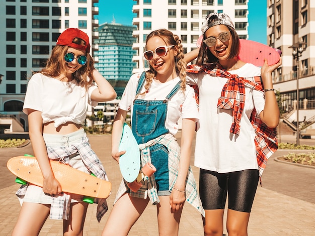 Three young smiling beautiful girls with colorful penny skateboards.