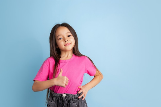 Free photo thumb up, nice gesture. caucasian little girl's portrait on blue wall. beautiful female model in pink shirt.