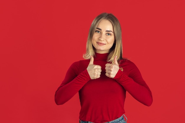 Free Photo thumbs up. monochrome portrait of young caucasian blonde woman isolated on red wall. beautiful female model in shirt. human emotions, facial expression, sales, ad concept. youth culture.