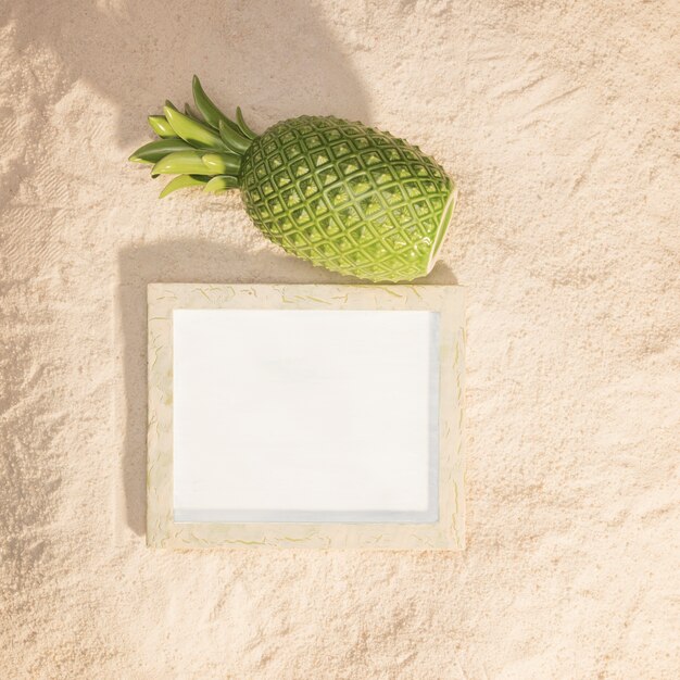 Timber picture frame and pineapple on sand