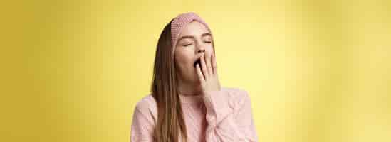 Free photo time to bed portrait of tired cute sleepy girlfriend wearing sweater knitted headband yawning cute with closed eyes opened mouth covered with palm exhausted wanting sleep dreaming fall asleep