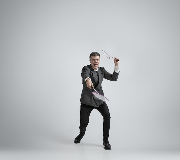 Free photo time for emotions. man in office clothes plays badminton with two racket on grey background