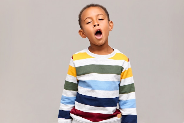 Time to go to bed. Fatigue and weariness concept. Weary cute dark skinned schoolboy opening mouth widely, yawning, feeling tired and sleepy, looks like dozing off, posing at blank wall