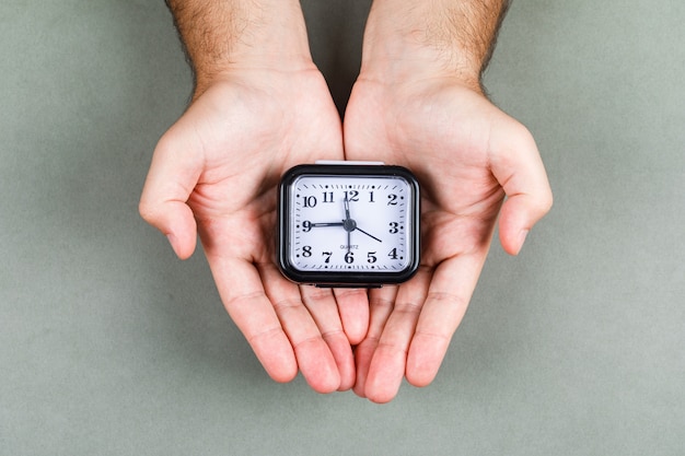 Free photo time management and clock ticking concept with clock on gray background top view. hands holding a clock. horizontal image