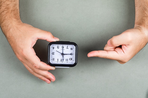 Free photo time management and clock ticking concept with clock on gray background top view. hands holding and pointing to the clock. horizontal image