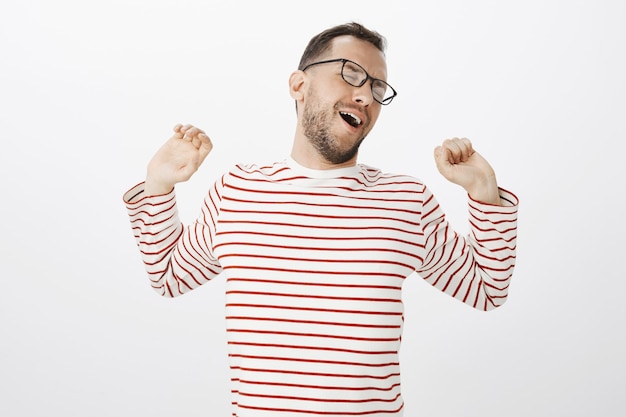 Free photo time to stratch after productive working day. portrait of tired relaxed attractive european man in striped shirt, pulling hands back while stratching and yawning